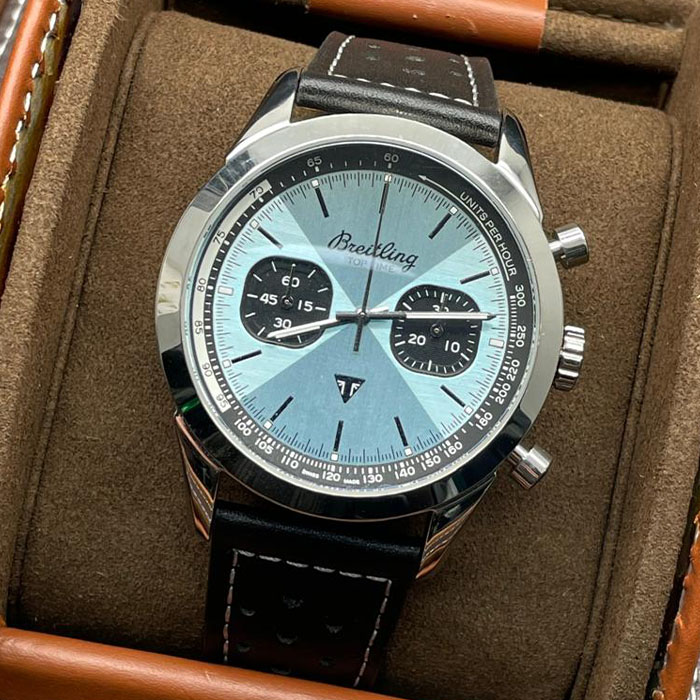 Reloj Breitling Top Time con carátula plateada, cronógrafo y correa de cuero negro con detalles blancos.