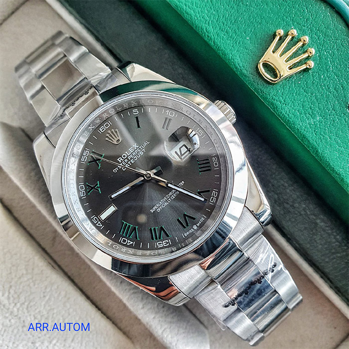 "Reloj Rolex Oyster Perpetual Datejust con esfera gris, números romanos verdes, ventana de fecha con lupa y brazalete de acero inoxidable.